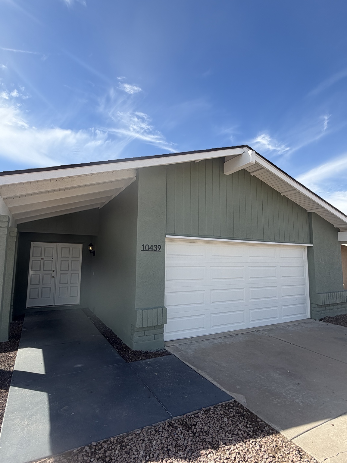 Green house facade with white roof trim and garage door
